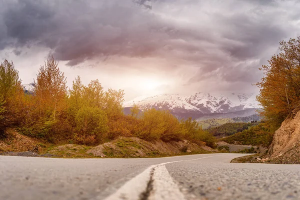Asphalt road in the mountains, autumn colors, cloud sky and sunset rays. — Stock Photo, Image