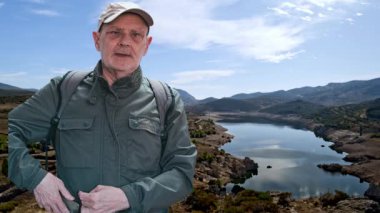 Sırt çantalı bir adam, berrak bir gökyüzünün altında dağlarla çevrili sakin bir gölü seyretmekten zevk alır. Huzuru, doğayı ve dışarıyı keşfetmek için mükemmel bir an..