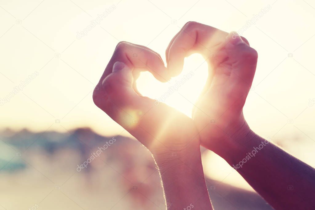 female hands showing heart sign against sunny sky