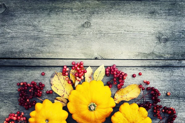 カボチャや木製のテーブルの赤い果実と紅葉の背景 — ストック写真