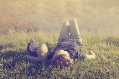 Mutlu yürümeye başlayan çocuk annesi güneşli park ile çim üzerinde yalan