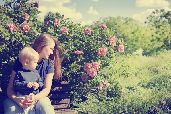 Happy Boy Sitting Bench Mother Blossoming Bushes Sunny Park — Stock Photo, Image