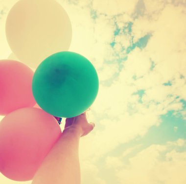 Gökyüzü arka plan üzerinde renkli büyük balonlar tutan el