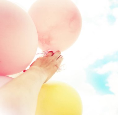 Gökyüzü arka plan üzerinde renkli büyük balonlar tutan el