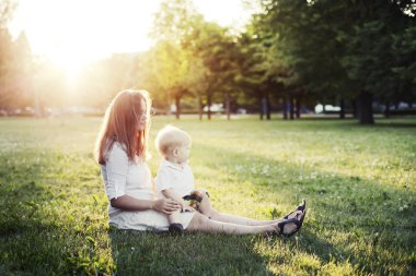 Mutlu anne ve küçük oğlu güneşli Park yeşil çimenlerin üzerinde dinlenme