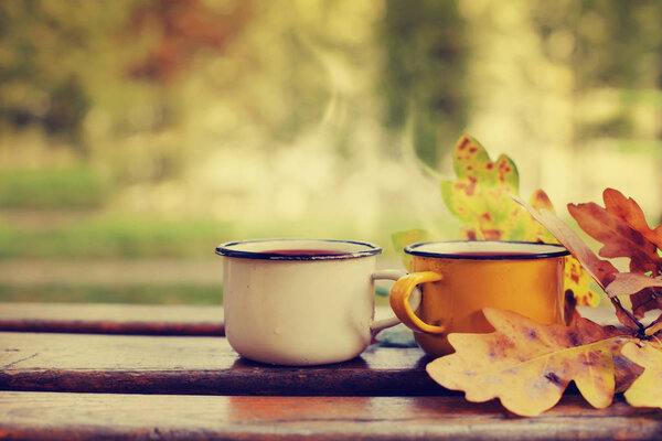 closeup view of two hot tea cups on wooden table with autumn entourage