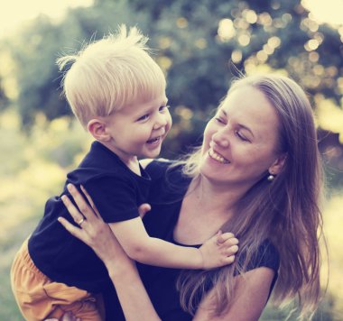 Gülümseyen güneşli parkta yürümeye başlayan çocuk oğlu ile oynayan kadın