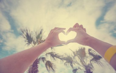 kalp şekli çerçeveleme batan güneşin batımında sahilde eller.