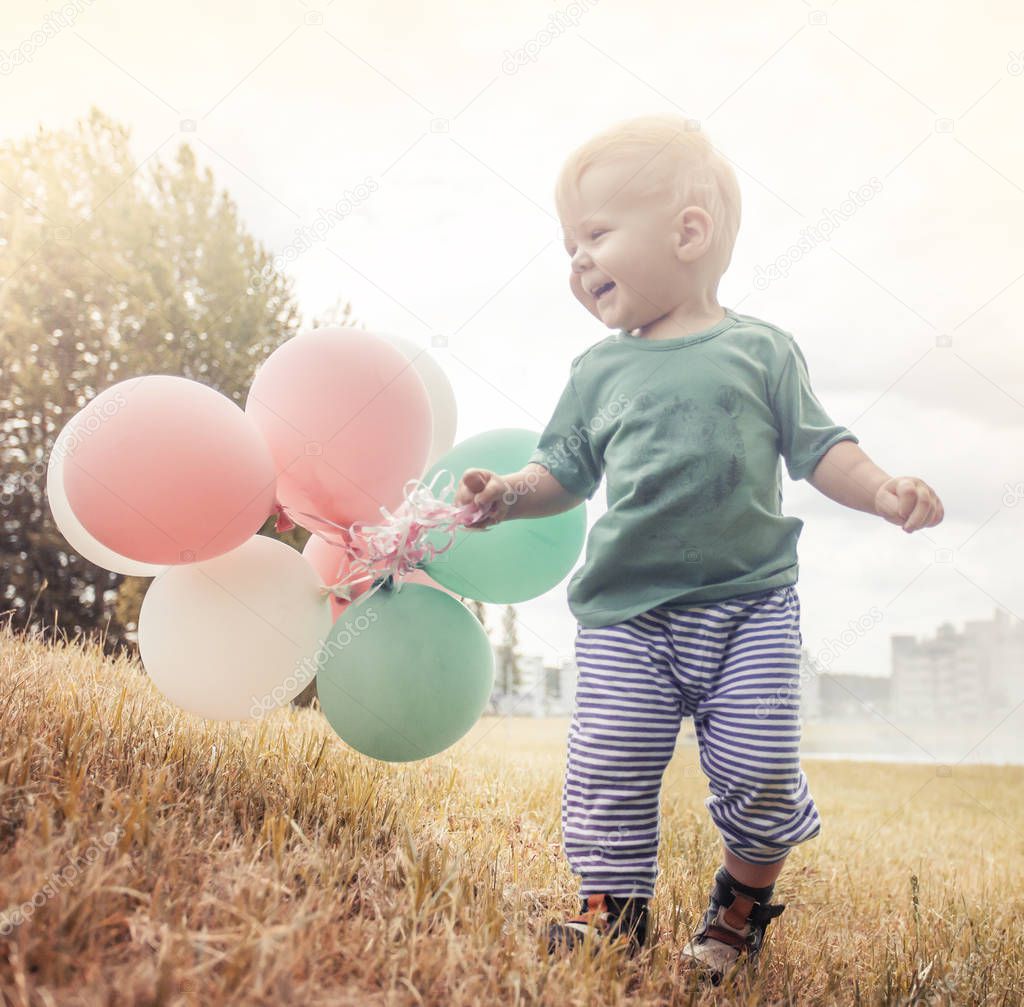 Happy child playing with colorful balloons in summer meadow