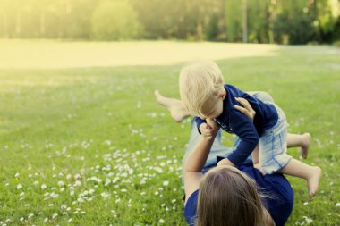 Güneşli park annesi ile yeşil çimenlerin üzerinde oynarken mutlu yürümeye başlayan çocuk