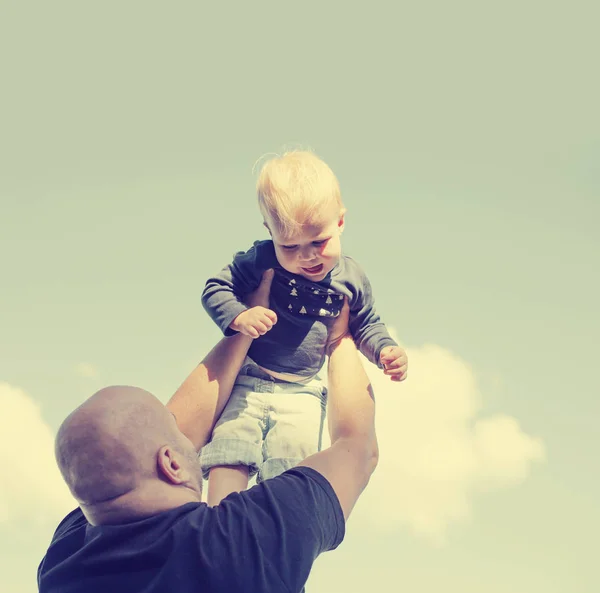 Father lifting baby boy in air while playing outdoors