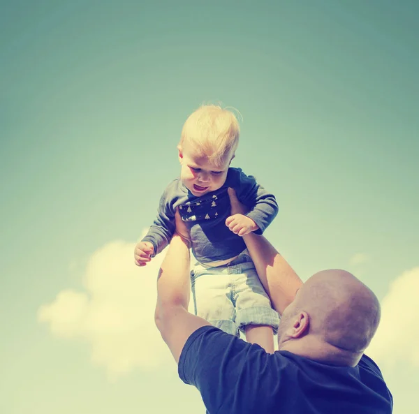 Father lifting baby boy in air while playing outdoors