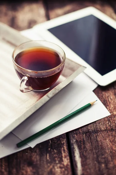 cup of hot tea on tray on wooden surface with digital tablet and stacked papers