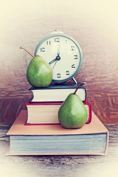 大钟与书籍和两个梨在木背景 — 图库照片