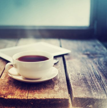 fincan sıcak çay ve dijital tablet ahşap yüzey üzerinde