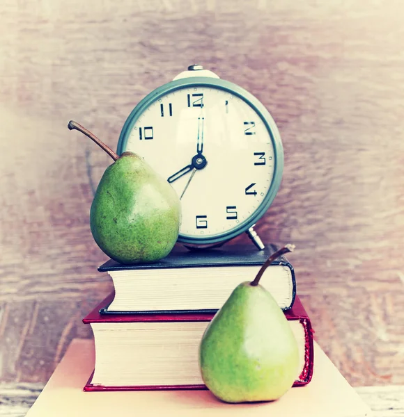 Big clock with books and two pears on wooden background