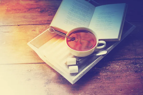 cup of hot tea and book on wooden surface