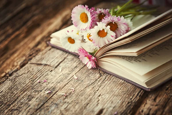 在木桌上打开的书上鲜艳的雏菊花束 — 图库照片