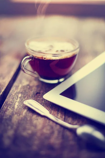glass cup of hot espresso and digital tablet on wooden surface