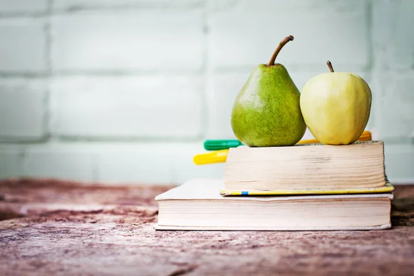 whole ripe apple and pear with books and markers on table