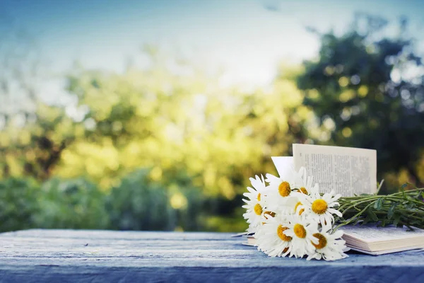 屋外の木製テーブルの上に開いた本の新鮮な鎮静の花束 — ストック写真