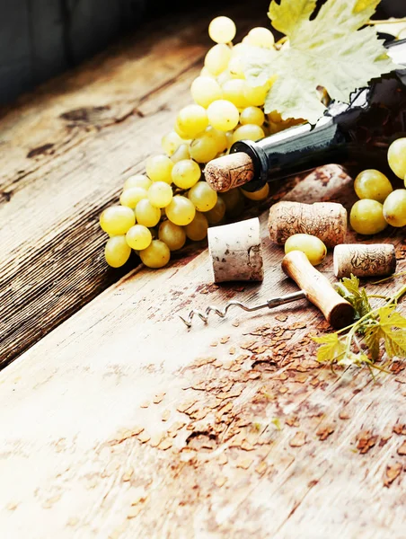 Bottle of white wine, grape and corks on wooden table