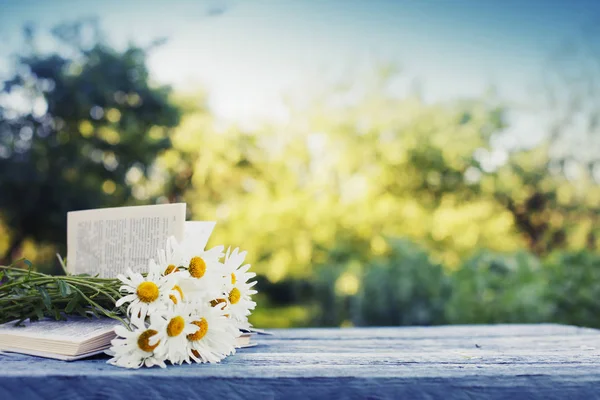 屋外の木製テーブルの上に開いた本の新鮮な鎮静の花束 — ストック写真