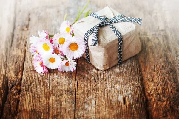 bright bouquet of daisies and gift box with ribbon on wooden table
