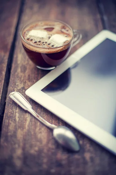 closeup view of coffee cup with ice and digital tablet lying on wooden table