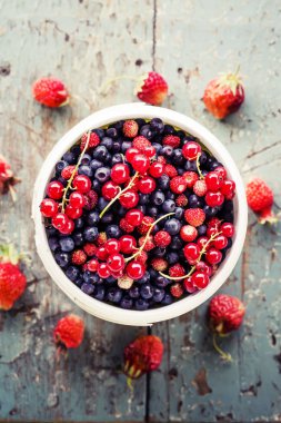 Kupa çilek ile eski püskü ahşap yüzeyde kırmızı kuş üzümü ile taze yaban mersini