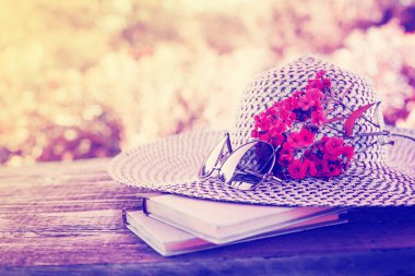 Kadın şapka gözlük, kitaplar ve bulanık doğa arka plan üzerinde pembe çiçekler