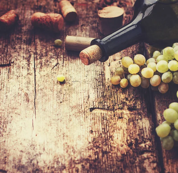 Bottle of white wine, grape and corks on wooden table