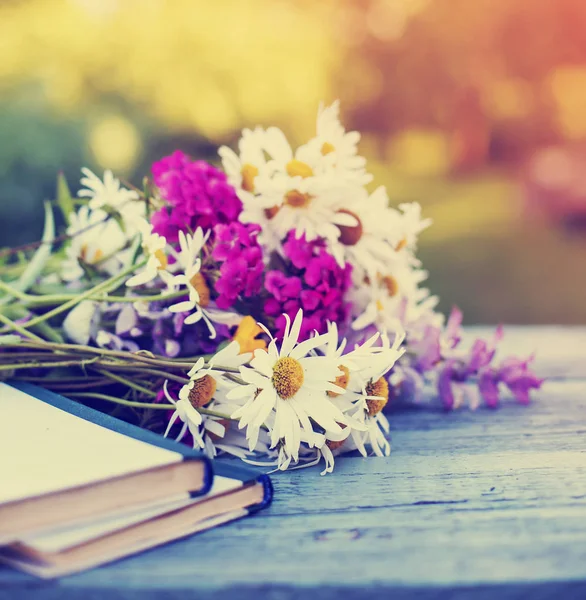 ビンテージの本のぼろぼろの木製テーブルの上の野生の花の花束 — ストック写真