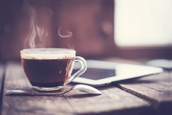 glass cup of hot espresso and digital tablet on wooden surface