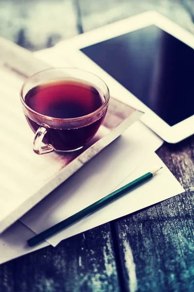 cup of hot tea on tray on wooden surface with digital tablet and stacked papers
