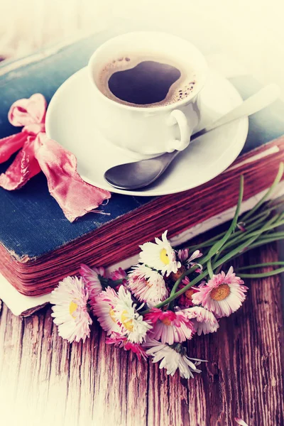 Tasty cup of coffee and flowers on books, wooden background