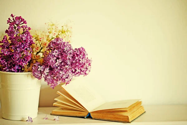 pink and white lilac flowers in bucket with old open book