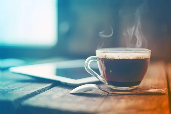 glass cup of hot espresso and digital tablet on wooden surface