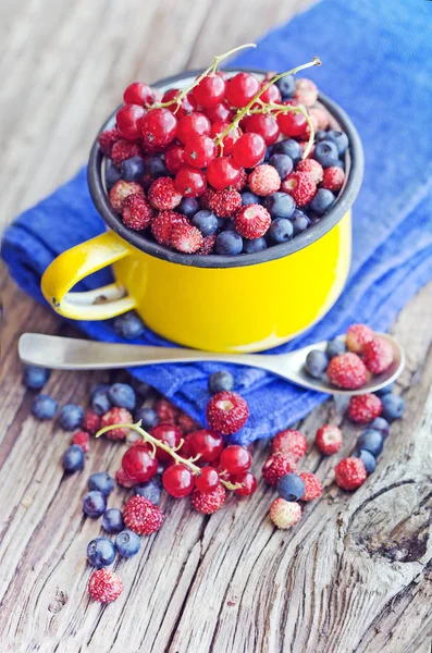 fresh blueberries, red currants and wild strawberries in mug on wooden surface