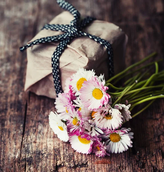 bright bouquet of daisies and gift box with ribbon on wooden table