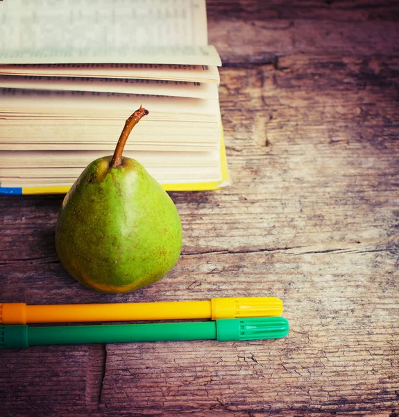 whole ripe pear with book and markers on table