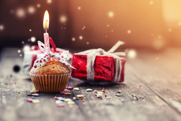 closeup view of cupcake with candle and colorful christmas decorations in vintage style over wooden background