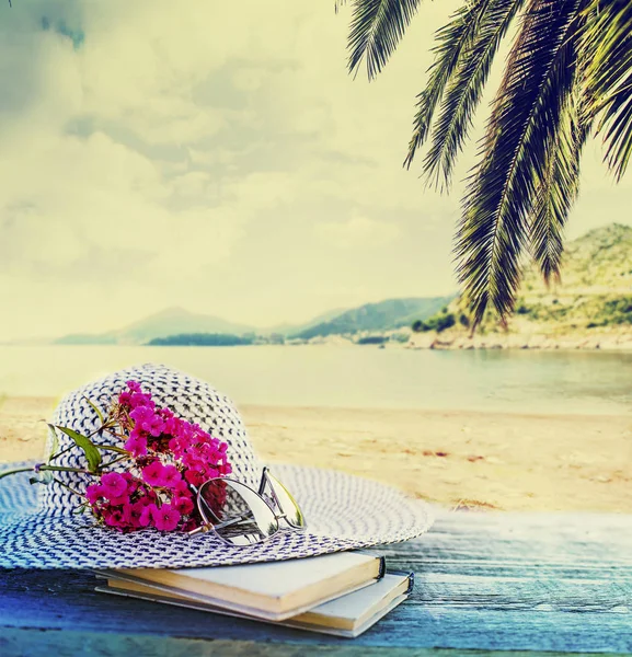 Female hat with glasses, books and pink flowers on blurred nature background