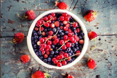 Kupa çilek ile eski püskü ahşap yüzeyde kırmızı kuş üzümü ile taze yaban mersini