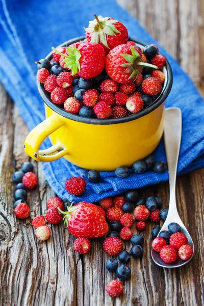fresh blueberries, strawberries and wild strawberries in mug on wooden surface