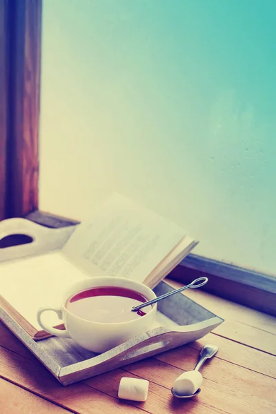 cup of hot tea and book on wooden surface