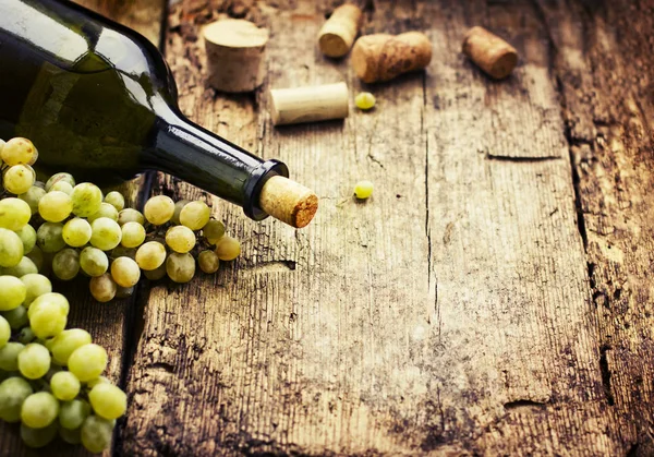 closeup view of green wine bottle with grapes on wooden table