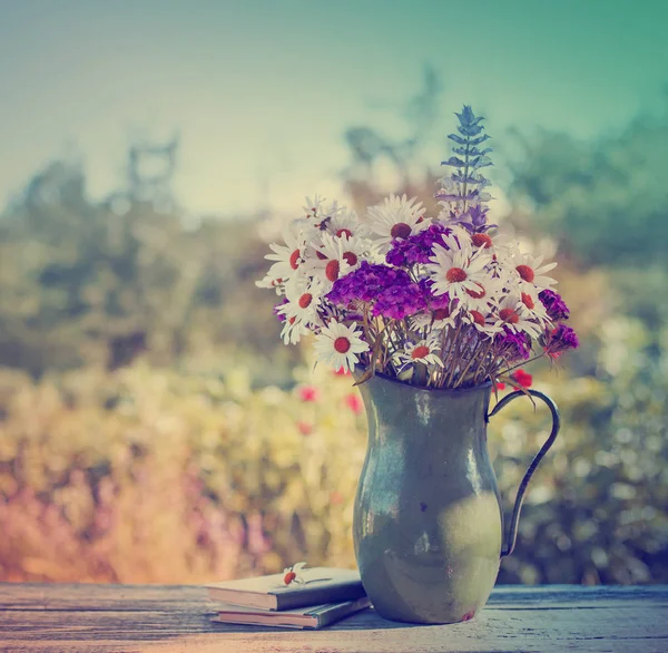 wild flowers in vase standing over wooden table with blurred nature background