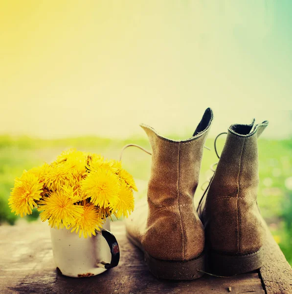 古い汚れたブーツを木の表面に金属のマグカップで黄色の花 — ストック写真