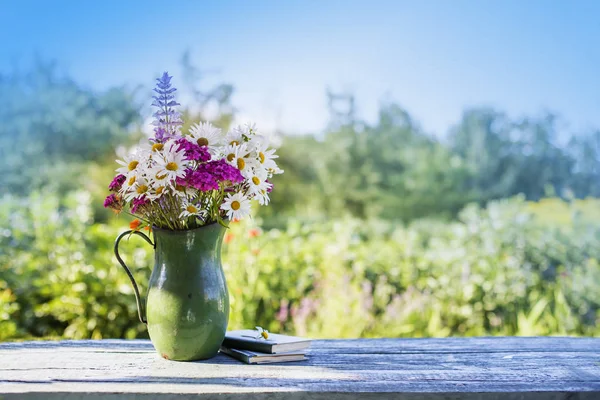 wild flowers in vase standing over wooden table with blurred nature background